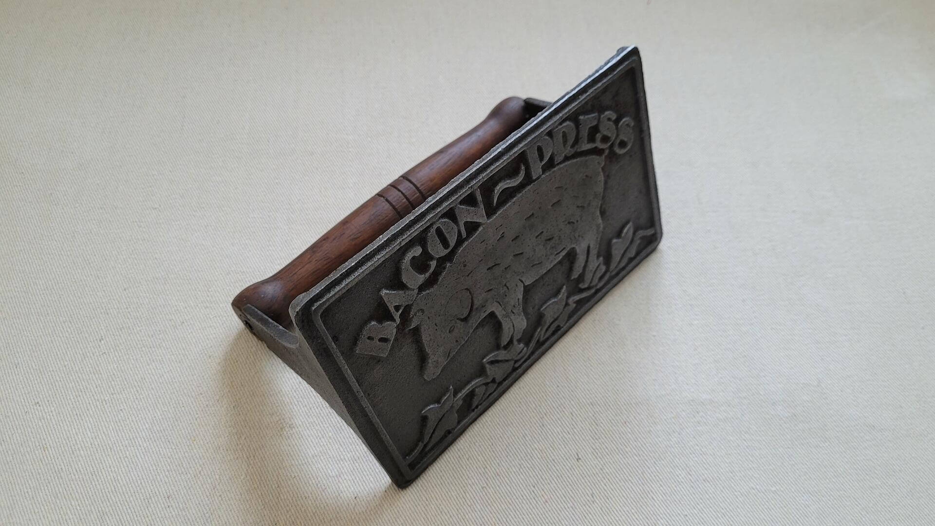vintage cast iron bacon press with wooden handle 4.5"x7" inches. Collectible rustic farmhouse kitchen tools featuring pig and vine design on the plate underside.