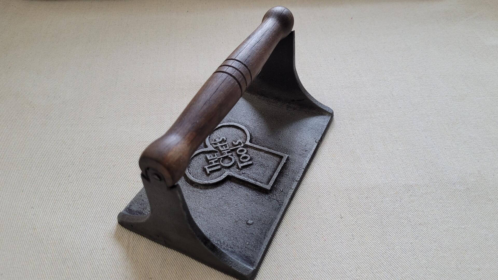 Vintage cast iron bacon press with wooden handle 4.5"x7" inches. Collectible rustic farmhouse kitchen tools featuring pig and vine design on the plate underside.