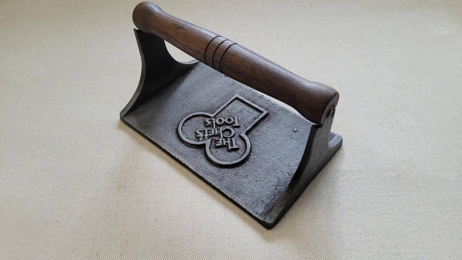 Vintage cast iron bacon press with wooden handle 4.5"x7" inches. Collectible rustic farmhouse kitchen tools featuring pig and vine design on the plate underside.